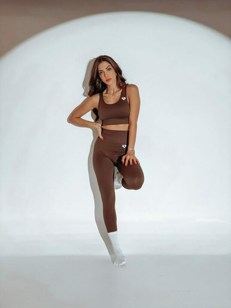 A woman is posing in a brown sports bra and leggings.
